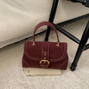 Detail showing burgundy textured leather bag with white contrast stitching and gold buckle