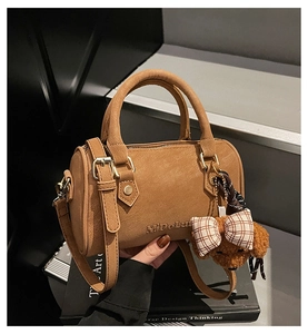 Detail of a brown suede Boston bag with adjustable strap and a teddy bear charm