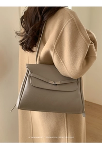 Close-up of taupe litchi grain leather tote with metal turn-lock and strap detail
