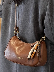 Brown leather crescent crossbody bag with wooden bead charm and adjustable strap