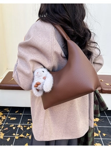 Brown lychee leather hobo bag with plush bunny charm on female model's shoulder
