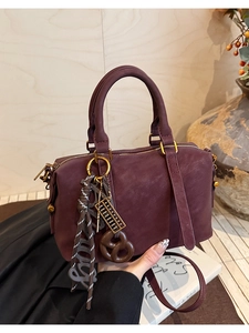 Detail of burgundy Boston bag showing leather texture, golden hardware and unique charms