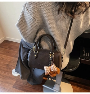Close-up of brown leather Boston bag featuring gold hardware and a cute teddy bear charm