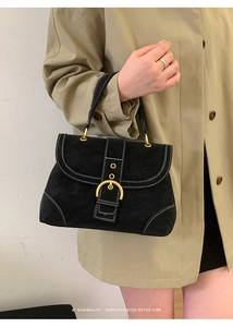 Detail of black suede handbag showing contrast white stitching and gold metal buckle