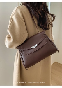 Detail of dark brown leather tote bag with silver buckle worn with a camel coat