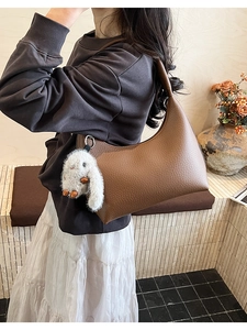 Detail shot of a dark brown litchi pattern leather hobo bag with a white rabbit charm
