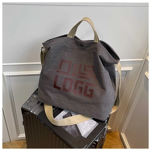 Close-up of deep gray canvas tote bag with artistic letter print on a silver suitcase