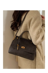 Detail of dark grey suede handbag with gold lock and key charm worn by a model