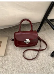 Macro view of burgundy square crossbody bag with a polished silver circular swivel lock