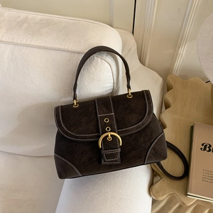 Close-up of brown suede mini bag with white stitching and gold clasp on sofa