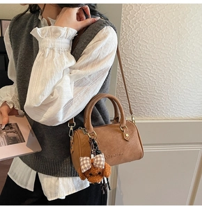 Detail view of a brown Boston bag with plush poodle charm and adjustable shoulder strap