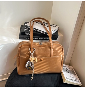 Brown leather shoulder bag with top double zipper and elegant heart charm on white background