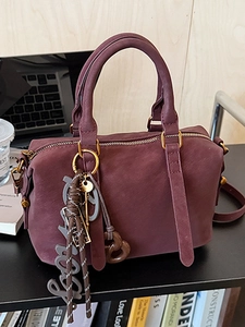 Burgundy Boston handbag with decorative Lucky charms on a stylish office desk setup