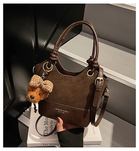 Detail of dark brown leather handbag featuring a plush bear charm on minimalist stairs