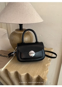 Detailed view of the semi-circular silver buckle on a black minimalist leather handbag