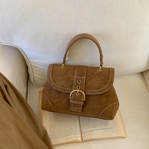 Close-up of vintage brown suede handbag with white stitching and bronze buckle