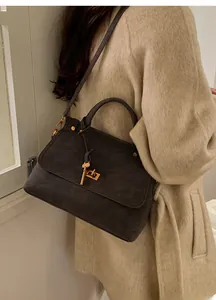 Detail of taupe suede crossbody bag with gold key lock shown on beige coat model