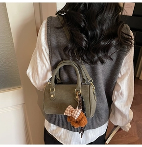 Olive green Boston bag with plush doll pendant shown from a back view on a model