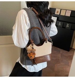 Detail of a retro color-block handbag with brown plush bear charm and crossbody strap
