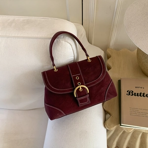Detailed close-up of wine red suede handbag with gold metal buckle and contrast stitching
