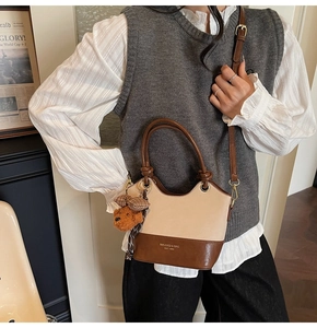 Detail of vintage beige leather handbag featuring brown contrast trim and teddy bear charm