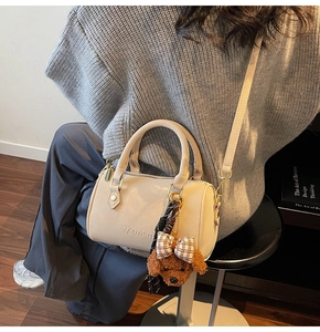 Detailed shot of cream Boston bag with plush dog charm and adjustable shoulder strap