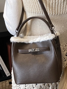 Brown leather bucket bag with white faux fur trim and silver lock, worn by a model