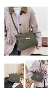 Detail view of dark green suede shoulder bag featuring classic gold metal lock and long strap