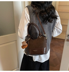 Detail view of brown bucket bag with plush bear charm and adjustable shoulder strap