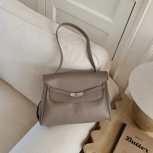 Detail of taupe pebbled leather tote bag with silver turn-lock on a cream sofa