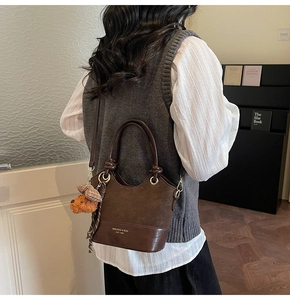 Detail of dark brown retro shoulder bag with plush bear charm and adjustable strap