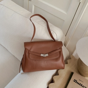 Detail of caramel leather tote bag showing soft litchi grain and silver twist lock on a sofa