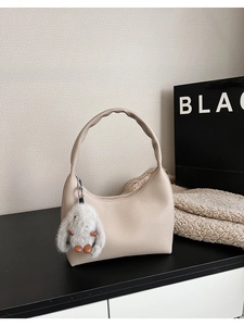 Detail of lychee textured cream moon bag featuring a soft grey plush rabbit charm accessory