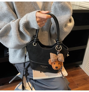 Detail view of black leather bucket bag featuring a plush bear charm and printed logo