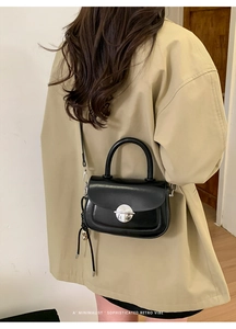 Detail view of black leather saddle bag with silver round buckle and tassel on tan coat