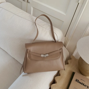 Close-up of brown litchi grain leather tote bag featuring a silver metal twist lock on a sofa