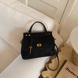 Detail of black faux leather handbag with gold twist lock and key charm on sofa