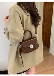 Detail of a brown leather crossbody bag with a round silver lock and woven tassel accent