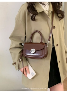 Detail of dark brown retro square bag featuring silver circular lock and metal tassel