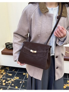 Detail of vintage brown leather crossbody bag with gold twist lock on winter coat