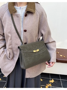 Close-up of olive green matte leather crossbody bag with metallic buckle on beige coat
