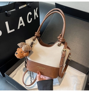 Detail view of two-tone bucket bag with knot handle and brown plush dog charm