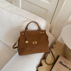 Detailed top view of a vintage brown leather handbag on a soft white sofa with metal lock