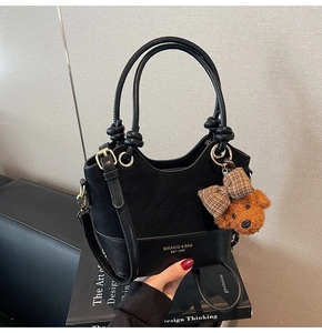 Detail of black leather handbag with gold embossed logo and cute brown bear keychain charm