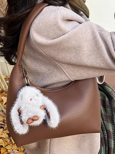 Brown litchi grain leather hobo bag with a white bunny plush charm in an autumn setting