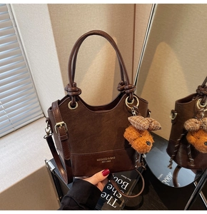 Detail view of brown textured bucket bag with elegant plush dog charm and gold hardware
