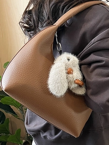 Brown textured leather hobo bag with a white rabbit plush charm worn over the shoulder