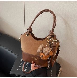 Close-up of brown patchwork handbag with logo and cute teddy bear charm detail