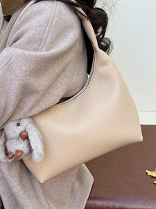 Minimalist beige pebble leather hobo bag with a plush bunny charm on wide shoulder strap