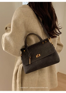 Detail view of charcoal grey suede square handbag with golden metal twist lock and rivets